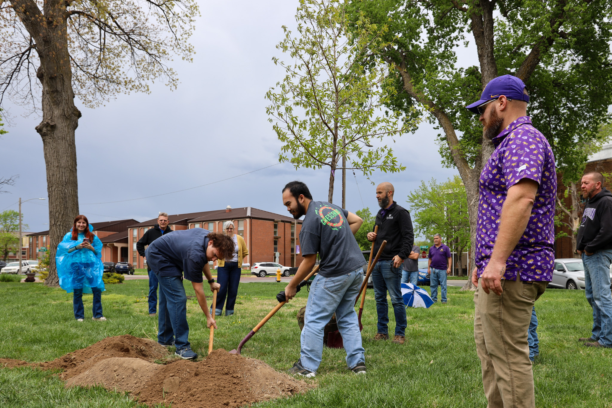 Two men digging to plant tree, others watching