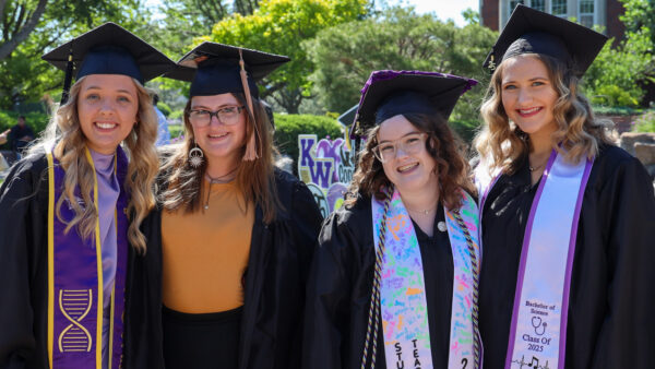 Group of graduates in cap and gown in front of Pioneer
