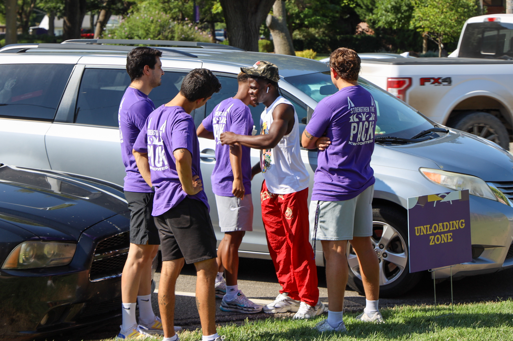 Group of men gathered near cars, two hugging