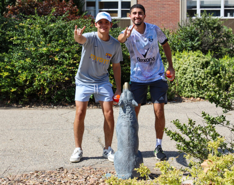 Two men standing by Coyote statue