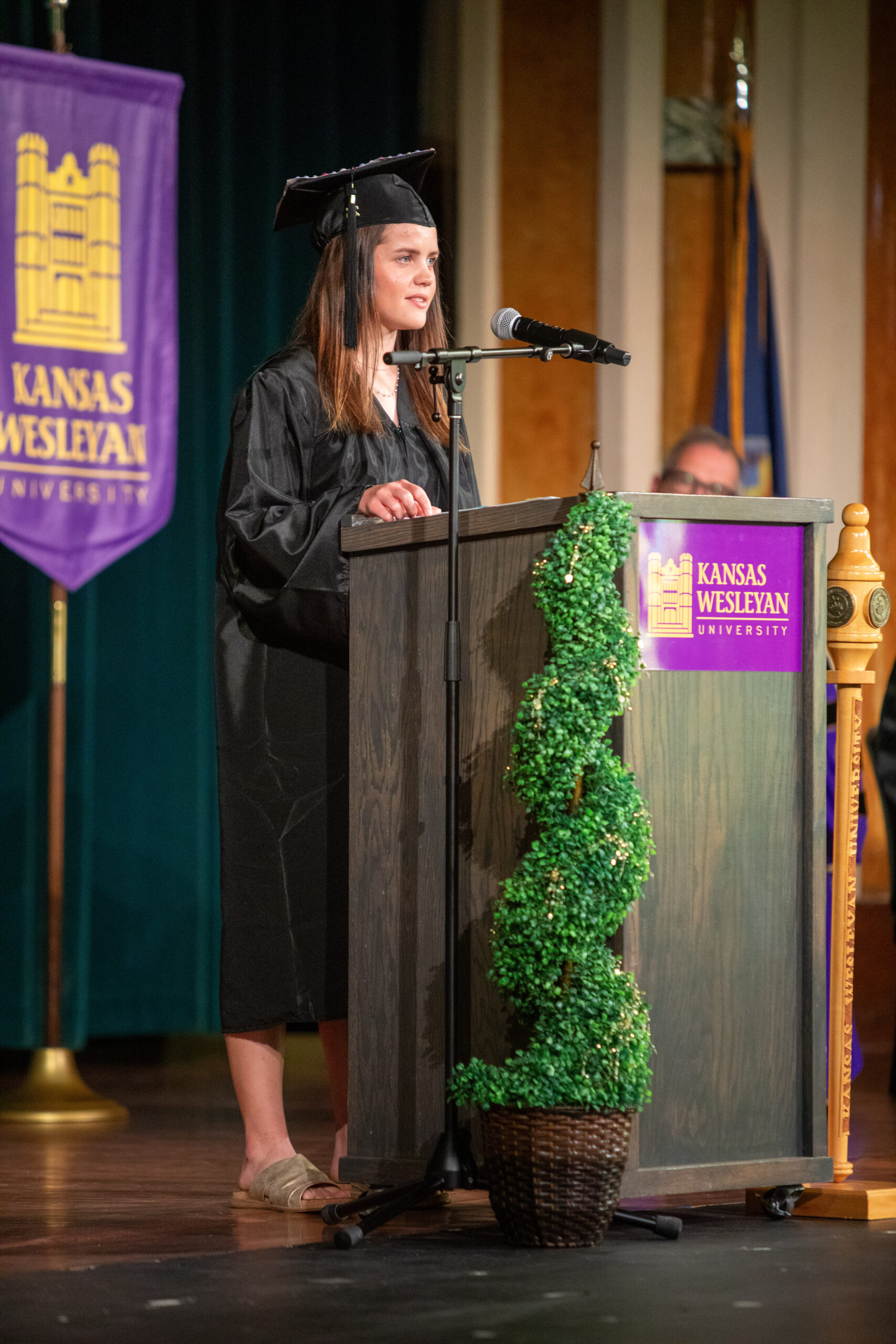 Woman at podium in cap and gown speaking