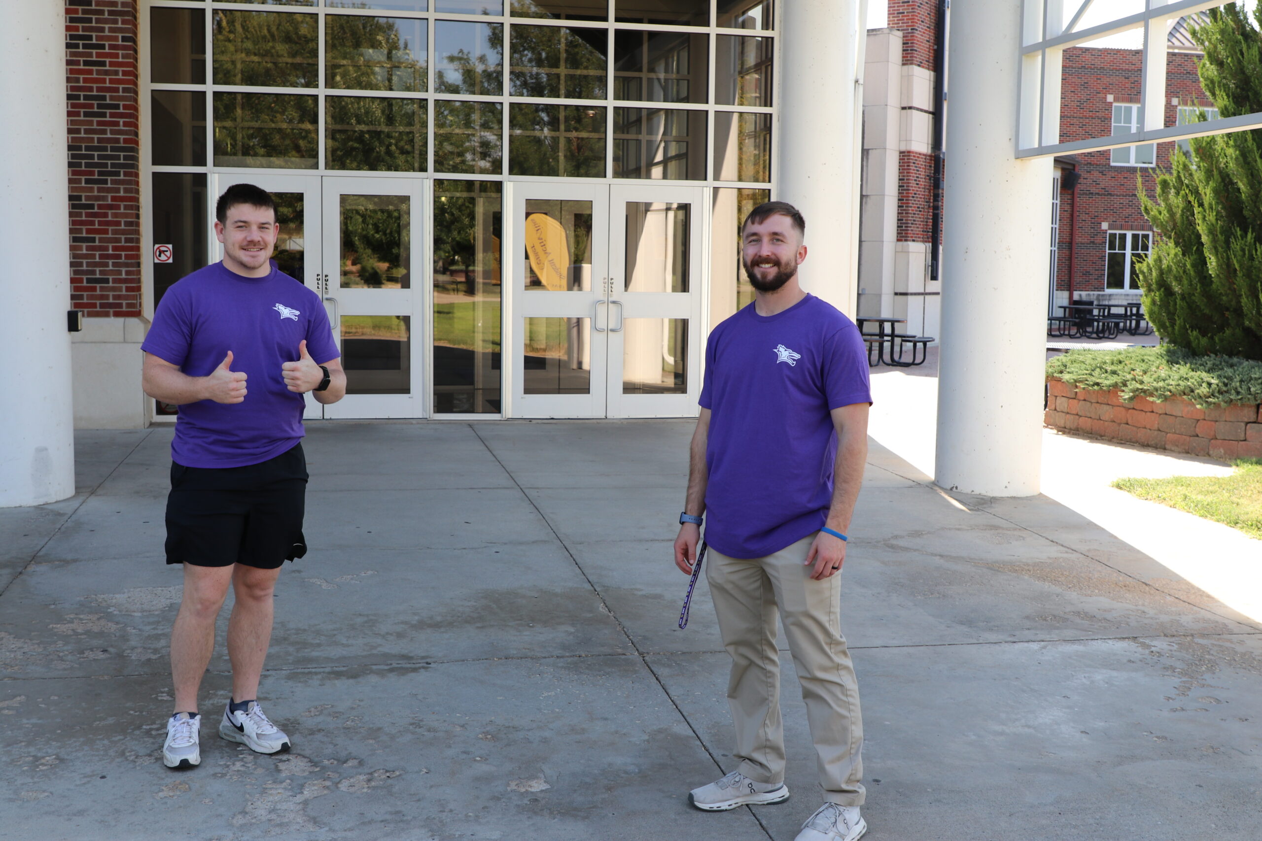 Two men standing outside of building giving thumbs up